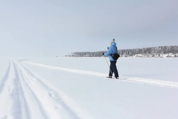 Kvinnan i en blå jacka skidåkning på snö över floden — Stockfoto