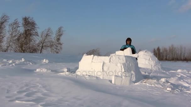 Человек строит иглу в снежную бурю зимой — стоковое видео