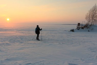 Gün batımında, Ob Nehri, Russiae donmuş nehrin üzerinde kayak adam