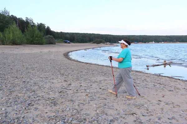 Nordic Walking - elderly woman is hiking along the river in the evening