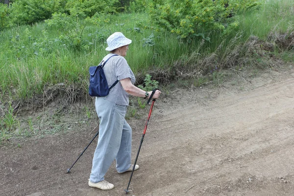 Nordic Walking-ηλικιωμένοι γυναίκα σε ένα ριγέ μπλούζα ανηφόρα — Φωτογραφία Αρχείου