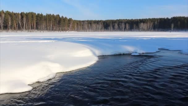 El agua que fluye fuera del lago entre la nieve en la puesta del sol — Vídeo de stock