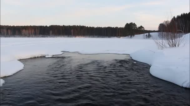 A água que flui para fora do lago entre a neve no pôr do sol — Vídeo de Stock