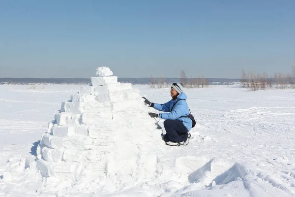 妇女在蓝色夹克建立一个冰屋在雪空地上 — 图库照片