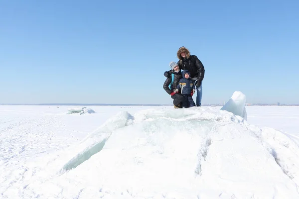 Glückliche Familie sitzt im Winter auf einer Eisscholle auf einem zugefrorenen Fluss — Stockfoto