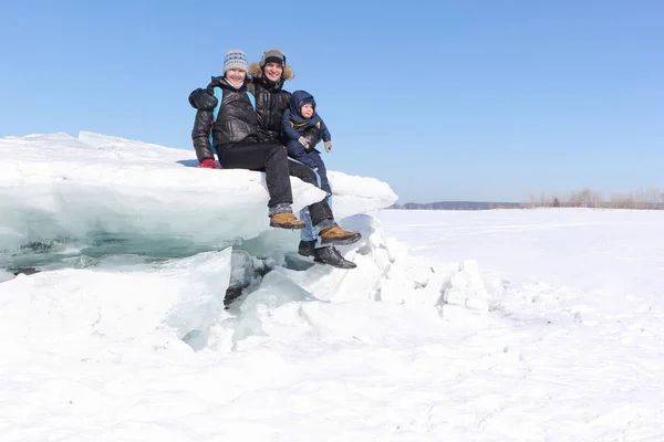 Glückliche Familie sitzt im Winter auf einer Eisscholle auf einem zugefrorenen Fluss — Stockfoto