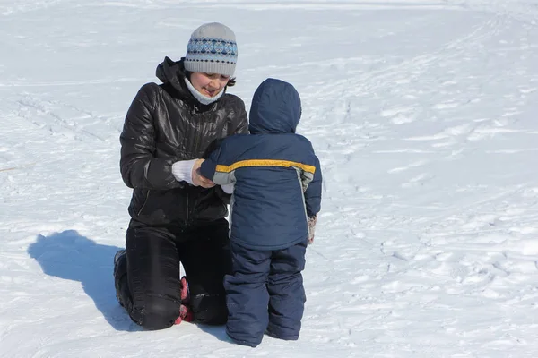 Vrouw corrigeren kleren aan een kind in de sneeuw in de winter — Stockfoto