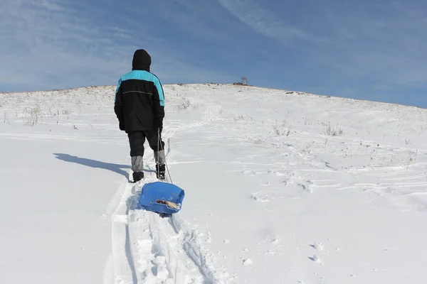 Hombre con chaqueta negra escalando una montaña con un trineo de plástico —  Fotos de Stock