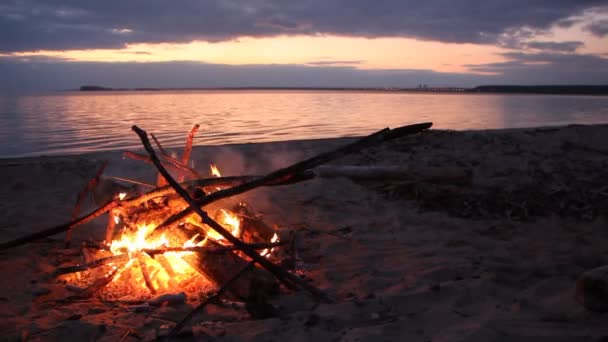 Feuer brennt am Ufer des Flusses bei Sonnenuntergang — Stockvideo