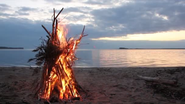 Fogueira na forma de uma tenda queimando na margem do rio no pôr do sol — Vídeo de Stock