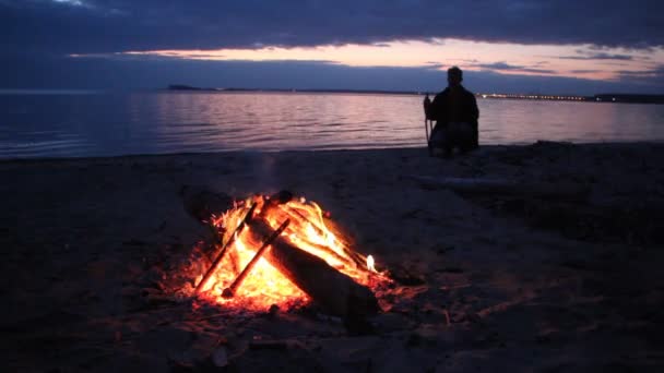 Hombre sentado junto al fuego cerca del río al atardecer, río Ob, Siberia , — Vídeos de Stock