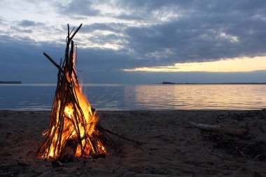 Nehir kıyısındaki günbatımı üzerinde yanan bir çadır şeklinde şenlik ateşi