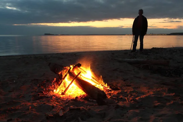 人站在河边篝火在日落时分 — 图库照片