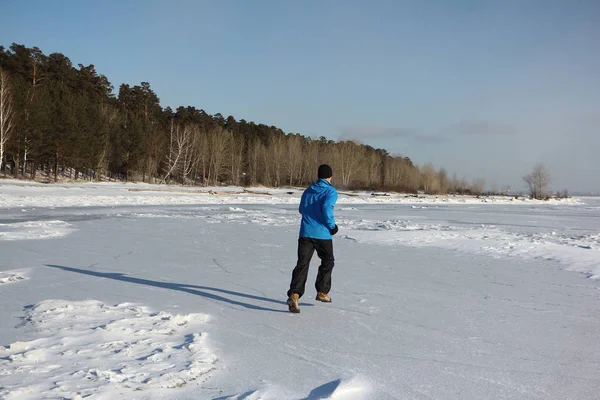 Man in een blauw jasje die dwars over het ijs van een bevroren rivier, O — Stockfoto