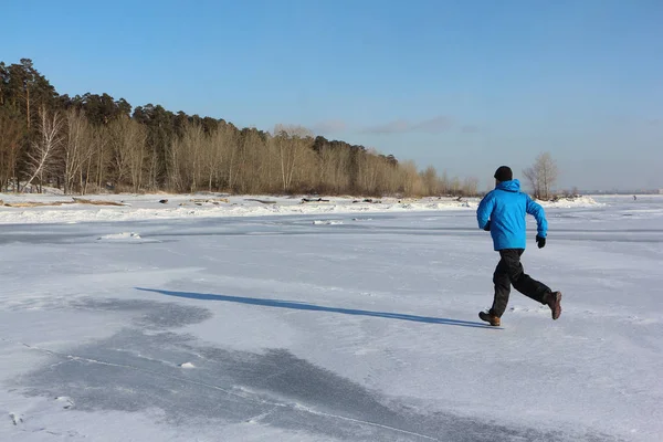 Man in een blauw jasje die dwars over het ijs van een bevroren rivier, — Stockfoto