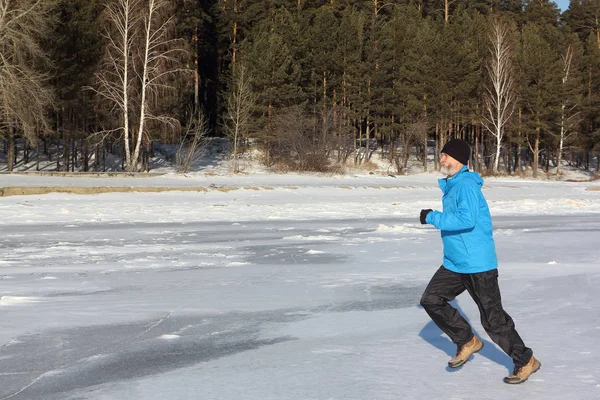 Mann in blauer Jacke läuft über das Eis eines zugefrorenen Flusses, o — Stockfoto