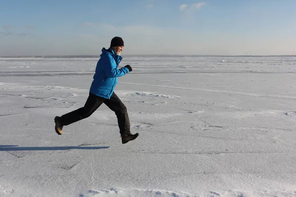 Mann in blauer Jacke läuft über das Eis eines zugefrorenen Flusses, o — Stockfoto
