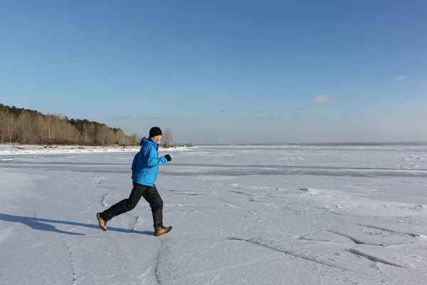 Man in een blauw jasje die dwars over het ijs van een bevroren rivier, O — Stockfoto