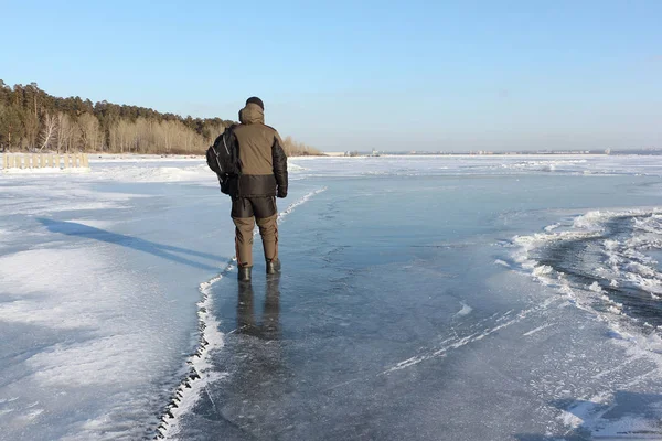 Homem em roupas quentes andando ao longo do gelo fino de um rio congelado — Fotografia de Stock