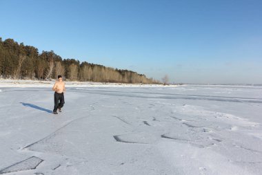 Man in a cap with a naked torso running across the ice of a river clipart