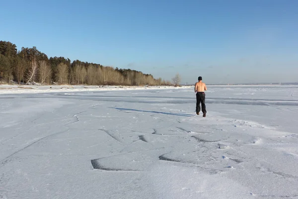 Man in a cap with a naked torso running across the ice of a river
