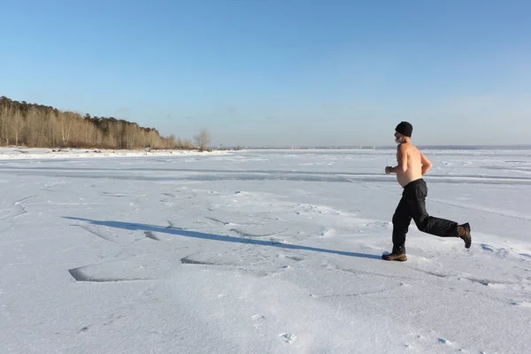 Man in een dop met een naakte torso die dwars over het ijs van een rivier — Stockfoto