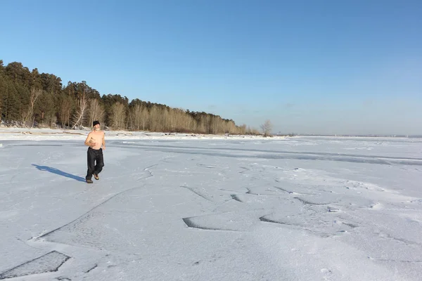 Un hombre con una gorra con un torso desnudo corriendo por el hielo de un río — Foto de Stock