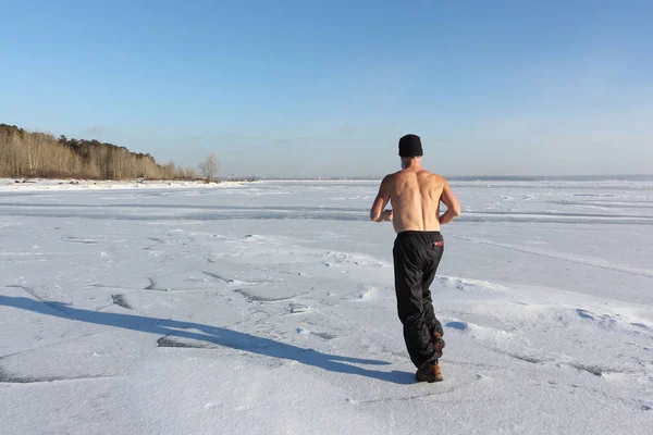 Man in een dop met een naakte torso die dwars over het ijs van een rivier — Stockfoto