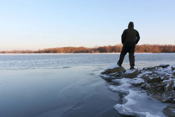 Человек, стоящий на камнях у замерзающей реки на закате — стоковое фото