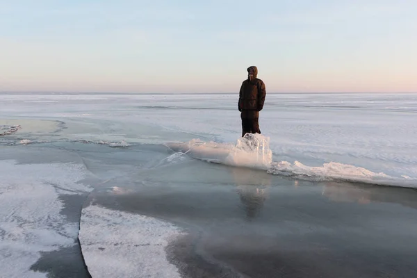 Hombre con ropa de abrigo parado sobre el hielo delgado de un río congelado — Foto de Stock