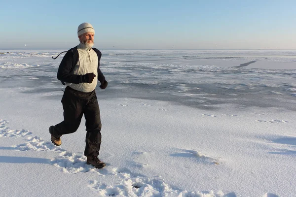 Пожилой человек в бежевом свитере, бегущий по льду замерзшего — стоковое фото