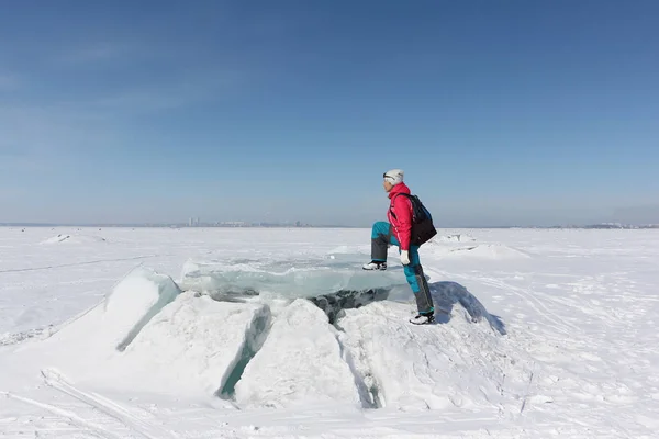 Счастливая женщина в красной куртке наступает на льдину на замерзшей реке — стоковое фото