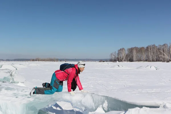 Lycklig kvinna i en röd jacka som kryper på ett isflak på en frusen flod — Stockfoto