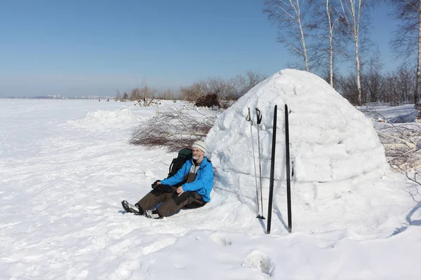 Hombre esquiador sentado junto a un iglú en un claro en el invierno —  Fotos de Stock