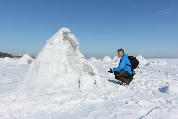 Hombre sentado a la entrada un iglú en un embalse nevado —  Fotos de Stock