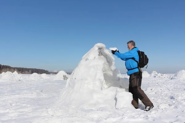 Man building an igloo on a snowy reservoir in winter — Stock Photo, Image
