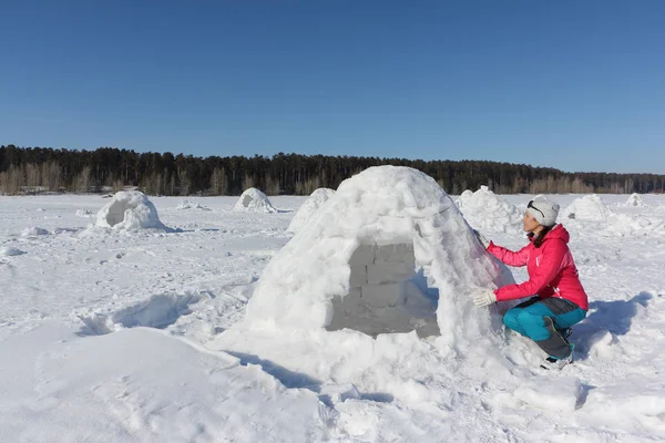 Mujer feliz una chaqueta roja construyendo un iglú en un claro de nieve —  Fotos de Stock