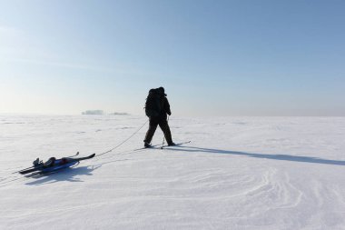 Kış vakti donmuş nehirde kayak yapan sırt çantalı bir adam.