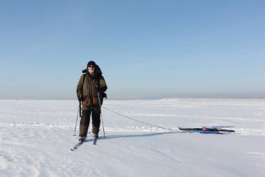 Kış vakti donmuş nehirde kayak yapan sırt çantalı bir adam.