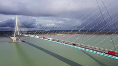 Fransa, Avrupa 'daki bir asma köprüde uçan araba ve kamyon trafiğinin hava görüntüsü. Pont de Normandy, Fransa 'nın kuzeyindeki büyük asma köprü Seine Nehri' ni gökkuşağı, Normandiya, Fransa 'da bulutlu bir gökkuşağı ile geçen köprü..