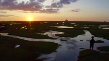 Le Mont-Saint-Michel 'in önündeki çayırlarda bir çocuk duruyor ve gün batımına bakıyor, Fransa