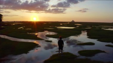 Le Mont-Saint-Michel 'in önündeki çayırlarda bir çocuk duruyor ve gün batımına bakıyor, Fransa