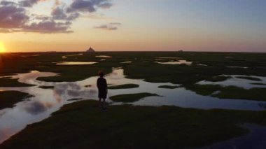Le Mont-Saint-Michel 'in önündeki çayırlarda bir çocuk duruyor ve gün batımına bakıyor, Fransa 