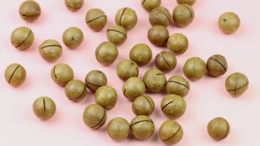 Çiğ, bütün macadamia fındıklarını soyup pembe arka planda sallamadı. Sağlıklı yiyecekler. Protein kaynağı. Yukarıdan görüntüle.