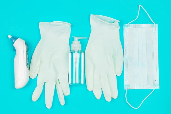 Máscara médica, termômetro, luvas de látex branco e gel higienizador de mão no fundo azul . — Fotografia de Stock