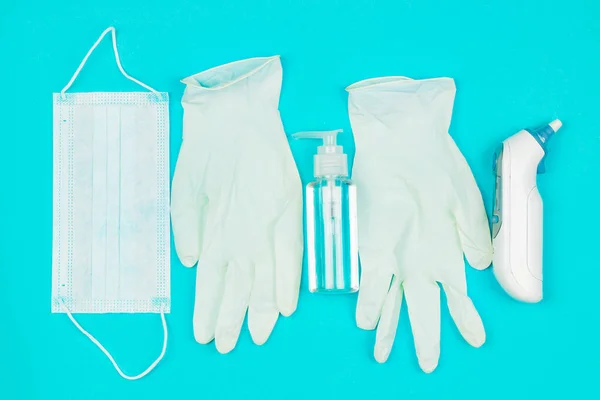 Máscara médica, termômetro, luvas de látex branco e gel higienizador de mão no fundo azul . — Fotografia de Stock