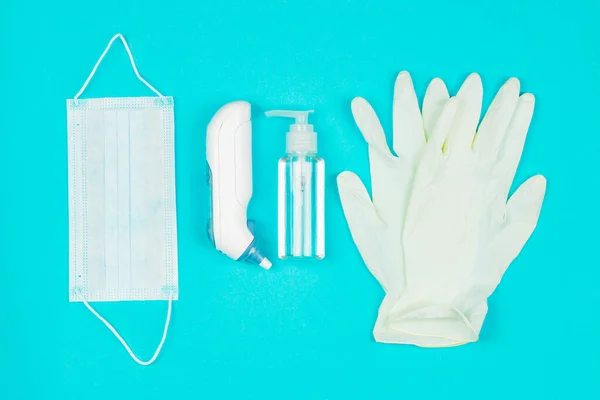 Masque médical, thermomètre, gants en latex blanc et gel désinfectant pour les mains sur fond bleu . Images De Stock Libres De Droits