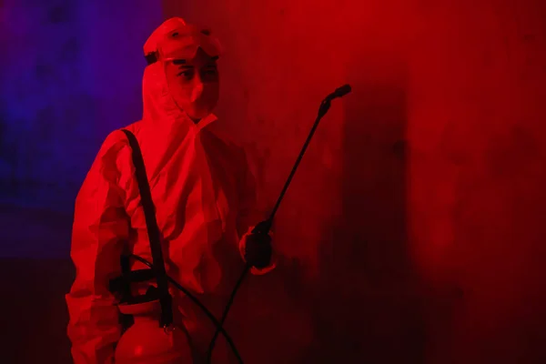 一名身穿化学防护服 戴着喷枪口罩的医生在一个有红色灯光的大房间里对考罗纳威斯进行治疗 — 图库照片