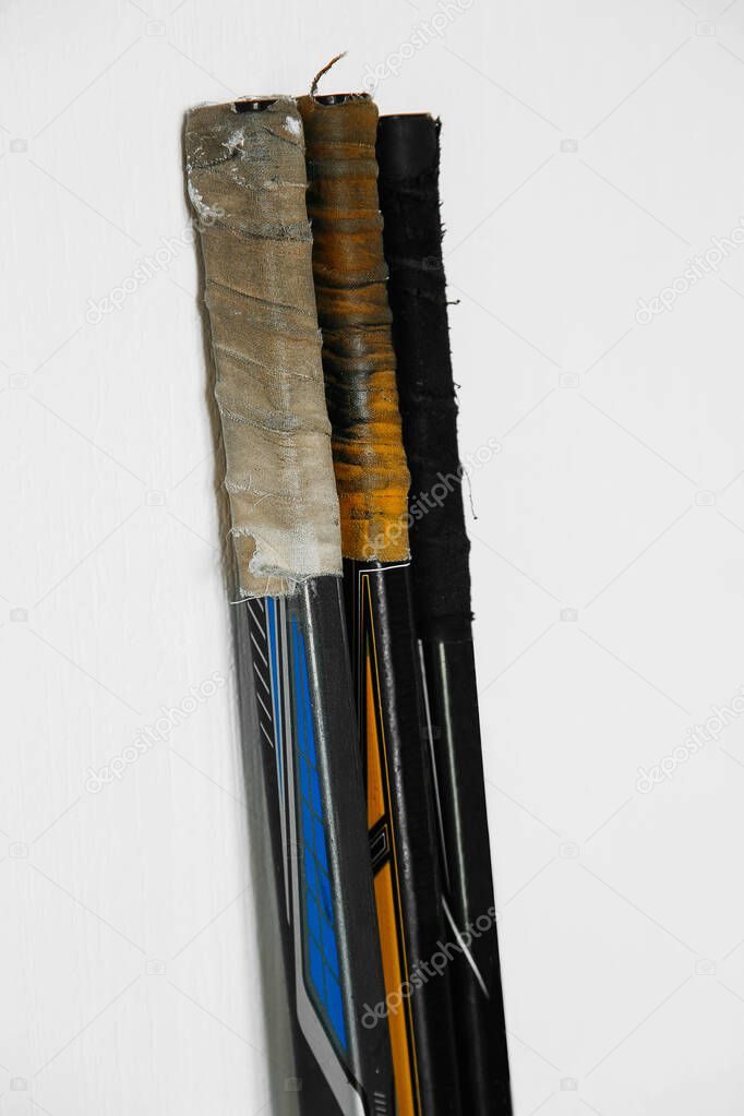Hockey sticks for playing with a puck on a white background stand in a row, the handles are rewound with colored tape with scuffs | EKATERINBURG, RUSSIA - 13.04.2020.