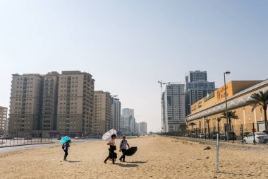 Bir kadın ve çocukları sıcak havada çölde yürür, yanan güneşten korunmak için güneş şemsiyeleri ile 124; BİRLİK ARAB EMIRATES, DUBAI - 17 Ekim 2017.